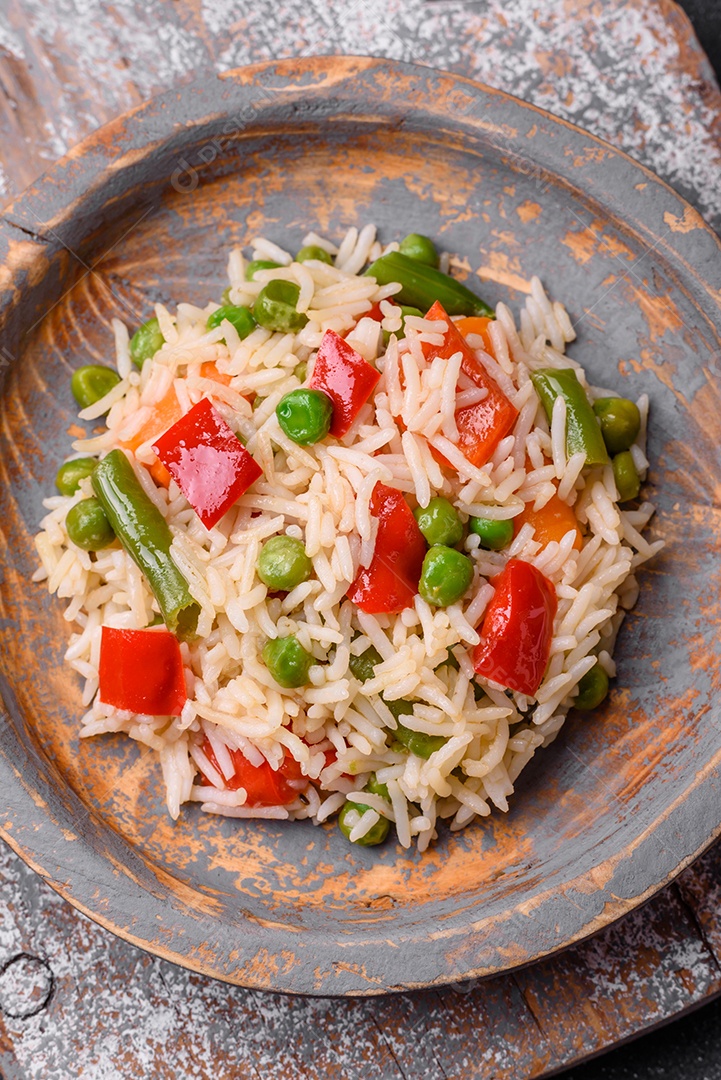 Delicioso arroz cozido com pimentão, ervilha, feijão de espargos e cenoura sobre um fundo de concreto texturizado