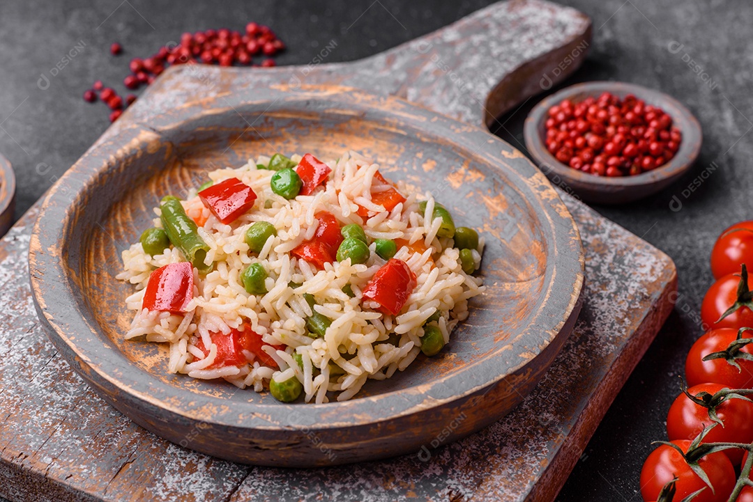 Delicioso arroz cozido com pimentão, ervilha, feijão de espargos e cenoura sobre um fundo de concreto texturizado