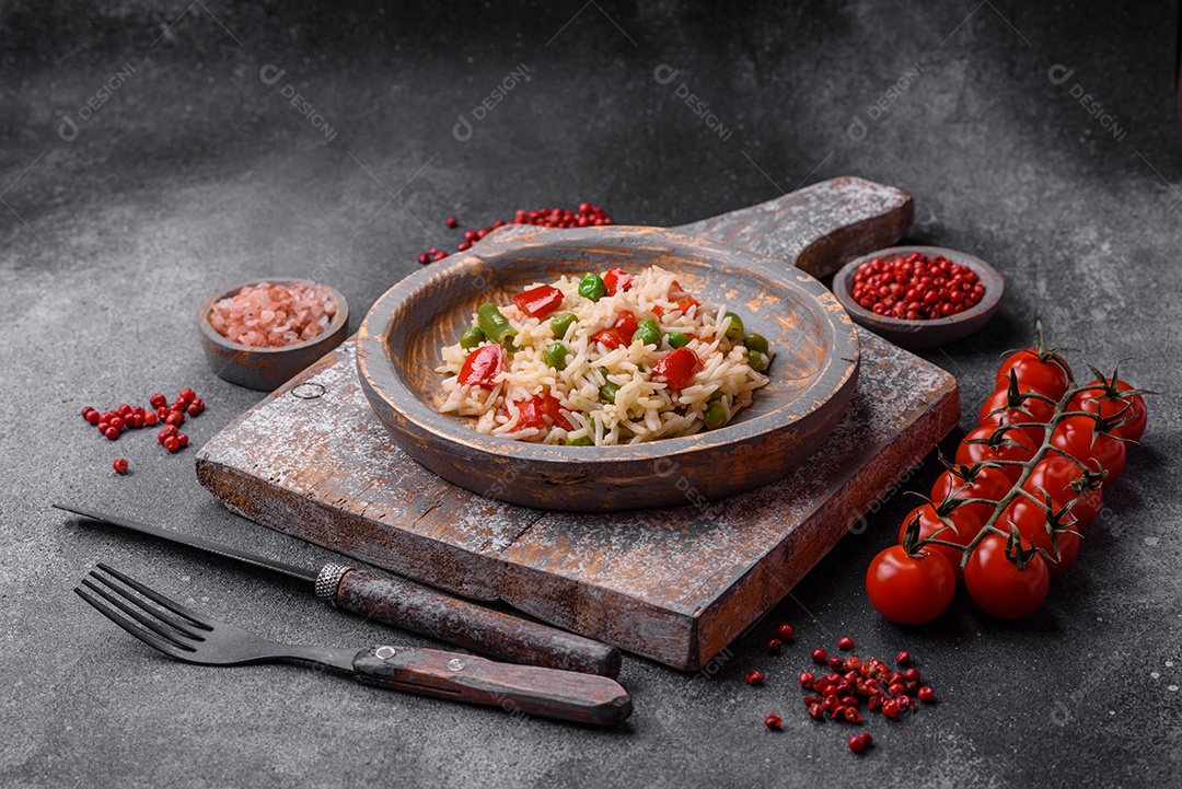 Delicioso arroz cozido com pimentão, ervilha, feijão de espargos e cenoura sobre um fundo de concreto texturizado