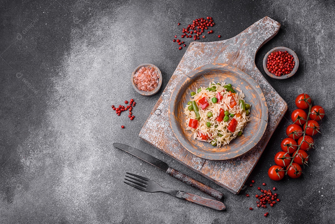 Delicioso arroz cozido com pimentão, ervilha, feijão de espargos e cenoura sobre um fundo de concreto texturizado
