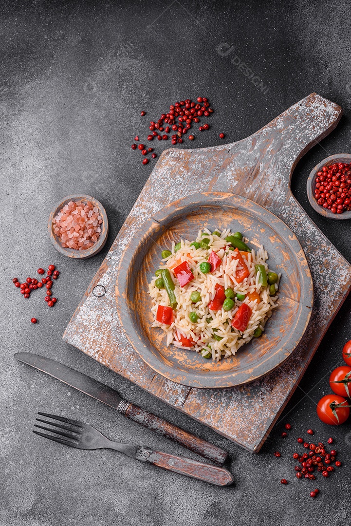 Delicioso arroz cozido com pimentão, ervilha, feijão de espargos e cenoura sobre um fundo de concreto texturizado