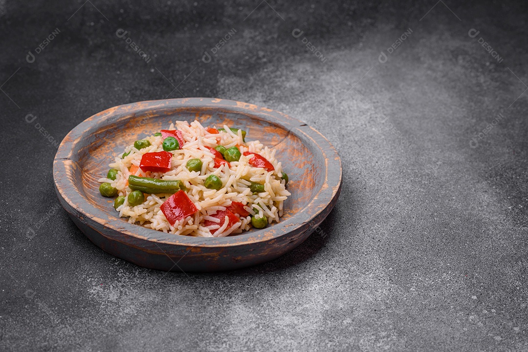 Delicioso arroz cozido com pimentão, ervilha, feijão de espargos e cenoura sobre um fundo de concreto texturizado