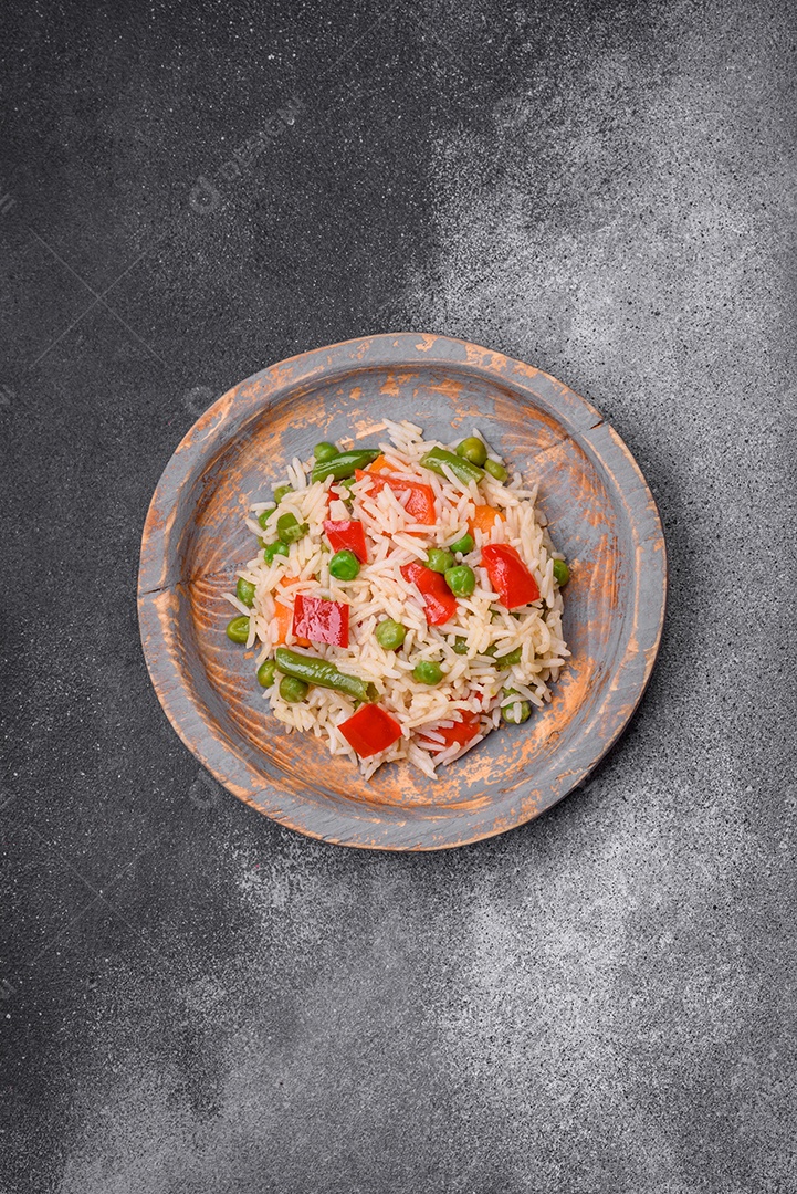 Delicioso arroz cozido com pimentão, ervilha, feijão de espargos e cenoura sobre um fundo de concreto texturizado