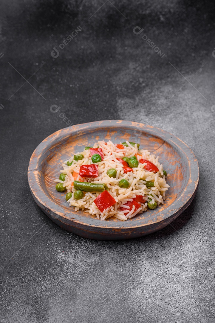 Delicioso arroz cozido com pimentão, ervilha, feijão de espargos e cenoura sobre um fundo de concreto texturizado