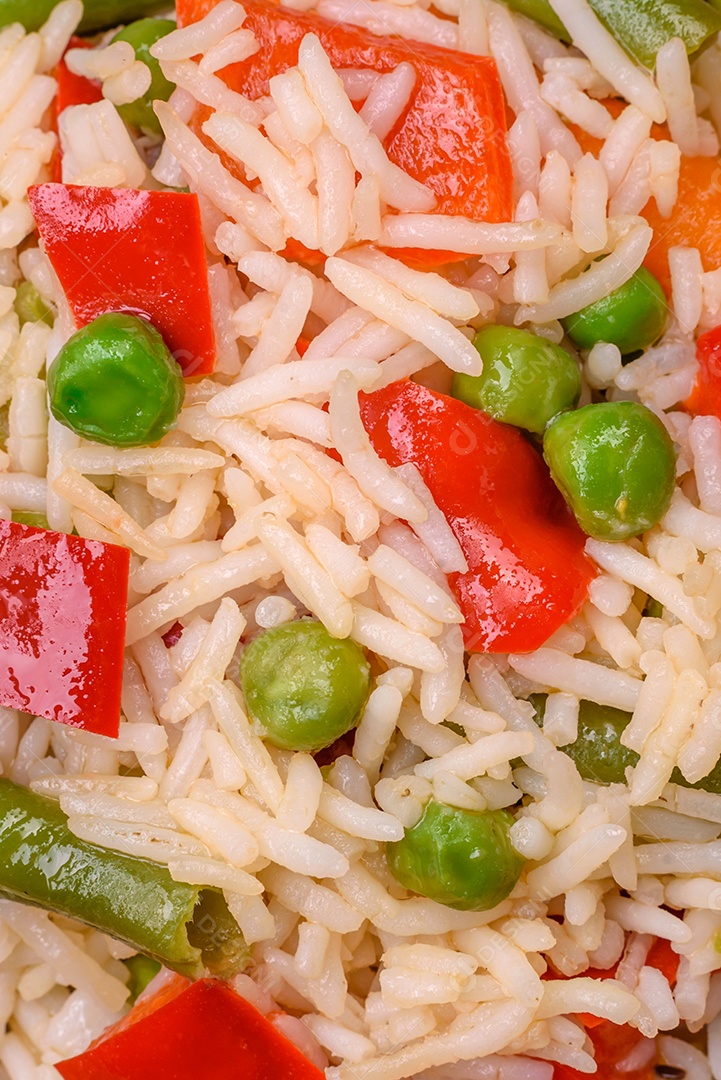 Delicioso arroz cozido com pimentão, ervilha, feijão de espargos e cenoura sobre um fundo de concreto texturizado