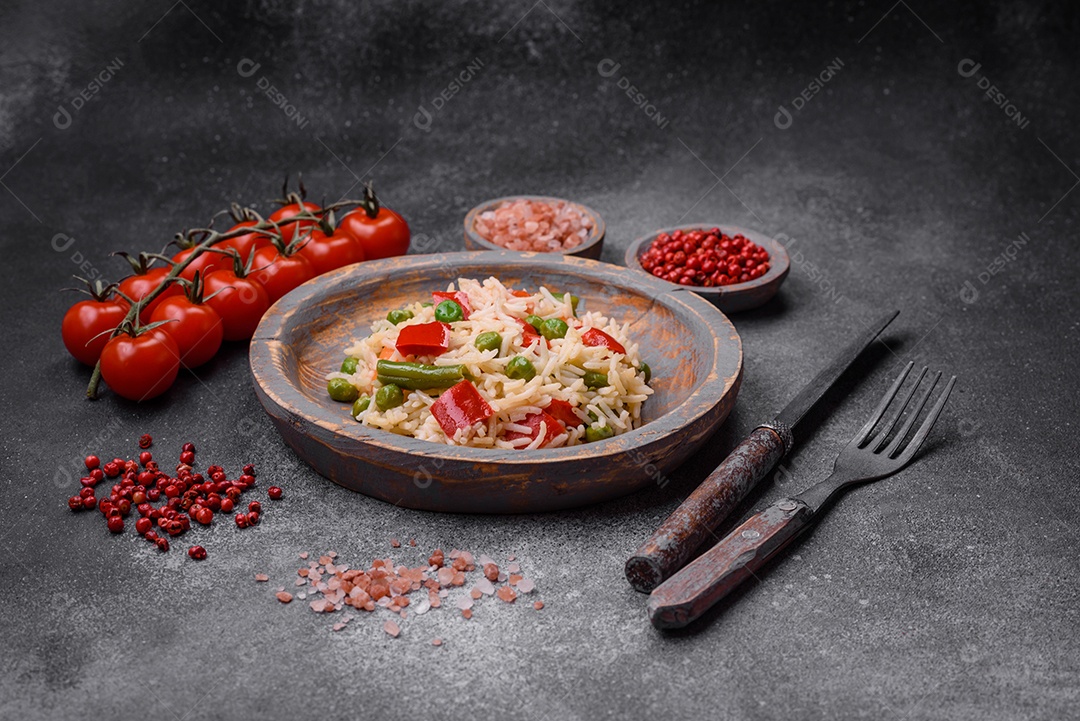 Delicioso arroz cozido com pimentão, ervilha, feijão de espargos e cenoura sobre um fundo de concreto texturizado