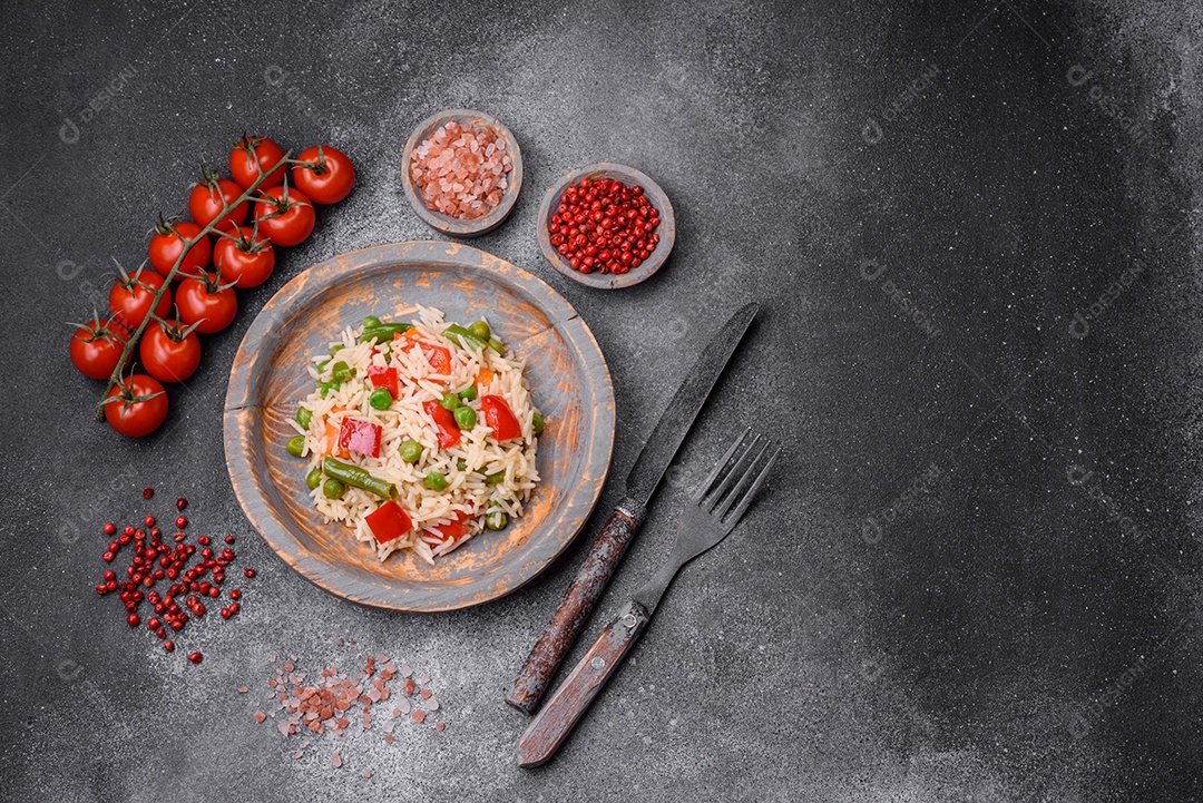 Delicioso arroz cozido com pimentão, ervilha, feijão de espargos e cenoura sobre um fundo de concreto texturizado