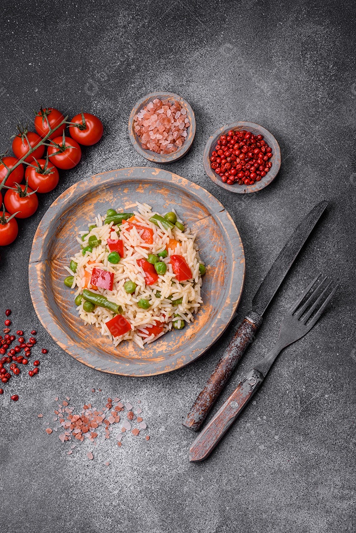 Delicioso arroz cozido com pimentão, ervilha, feijão de espargos e cenoura sobre um fundo de concreto texturizado