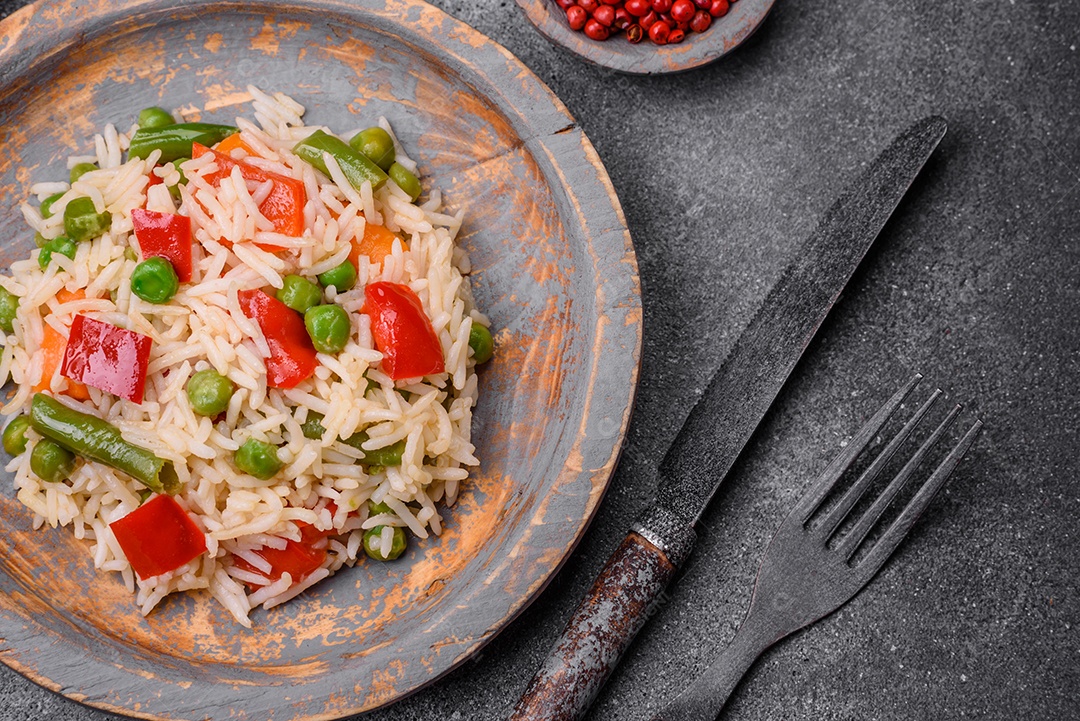 Delicioso arroz cozido com pimentão, ervilha, feijão de espargos e cenoura sobre um fundo de concreto texturizado
