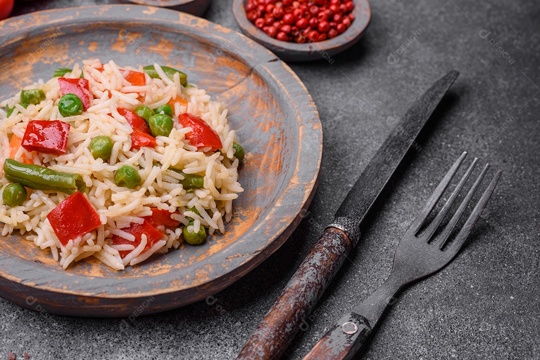 Delicioso arroz cozido com pimentão, ervilha, feijão de espargos e cenoura sobre um fundo de concreto texturizado