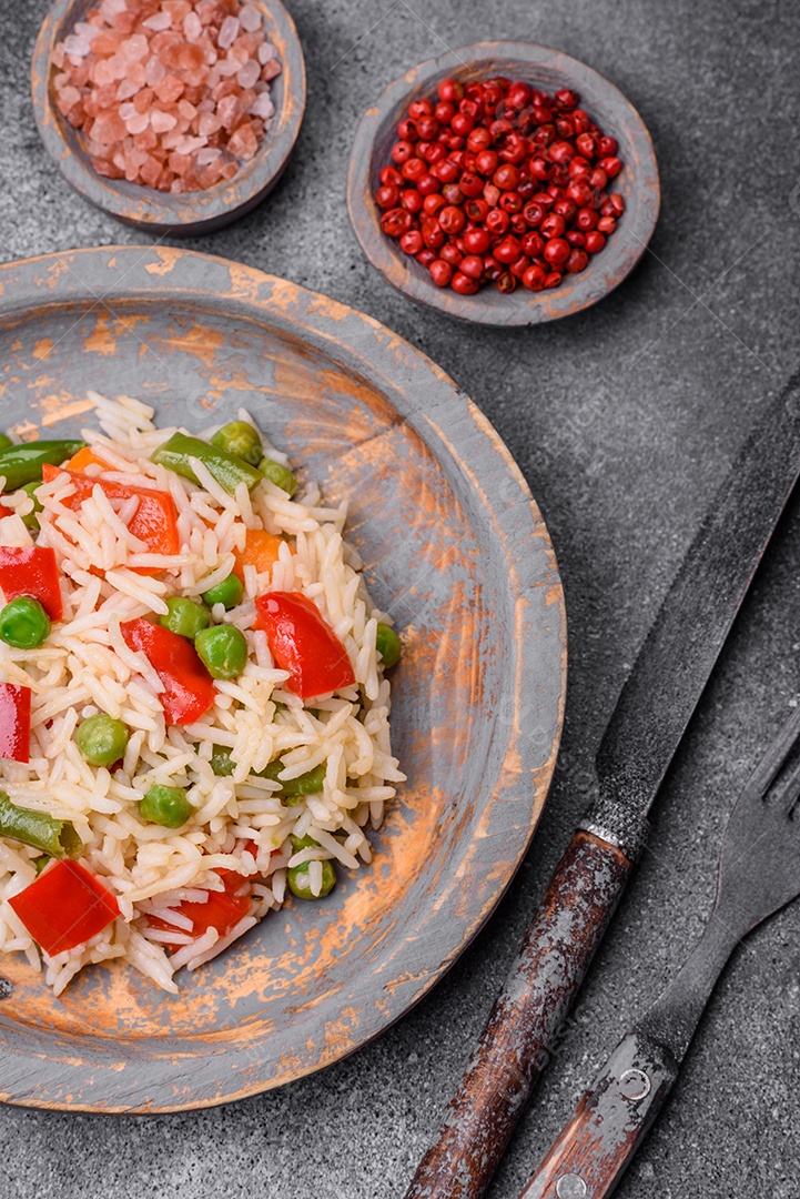 Delicioso arroz cozido com pimentão, ervilha, feijão de espargos e cenoura sobre um fundo de concreto texturizado