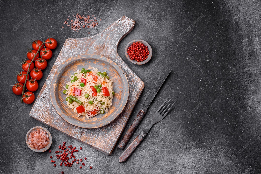 Delicioso arroz cozido com pimentão, ervilha, feijão de espargos e cenoura sobre um fundo de concreto texturizado