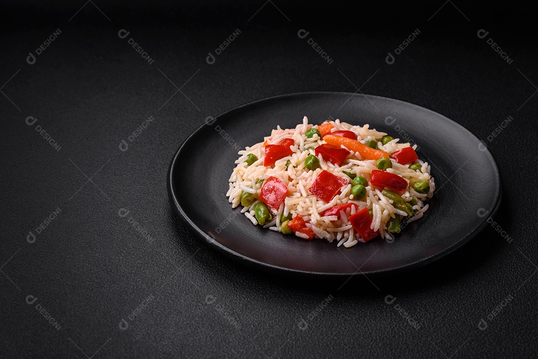 Delicioso arroz cozido com pimentão, ervilha, feijão de espargos e cenoura sobre um fundo de concreto texturizado