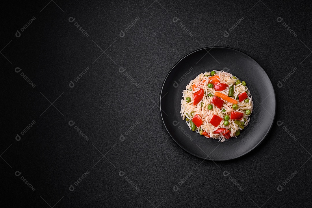 Delicioso arroz cozido com pimentão, ervilha, feijão de espargos e cenoura sobre um fundo de concreto texturizado