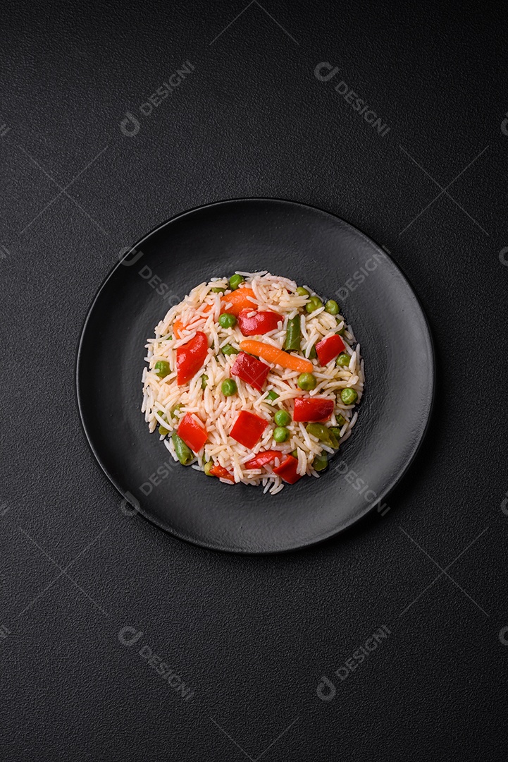 Delicioso arroz cozido com pimentão, ervilha, feijão de espargos e cenoura sobre um fundo de concreto texturizado