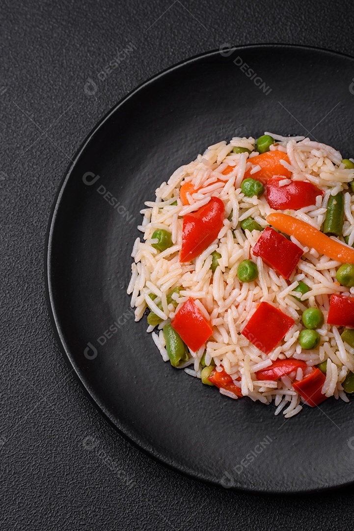 Delicioso arroz cozido com pimentão, ervilha, feijão de espargos e cenoura sobre um fundo de concreto texturizado