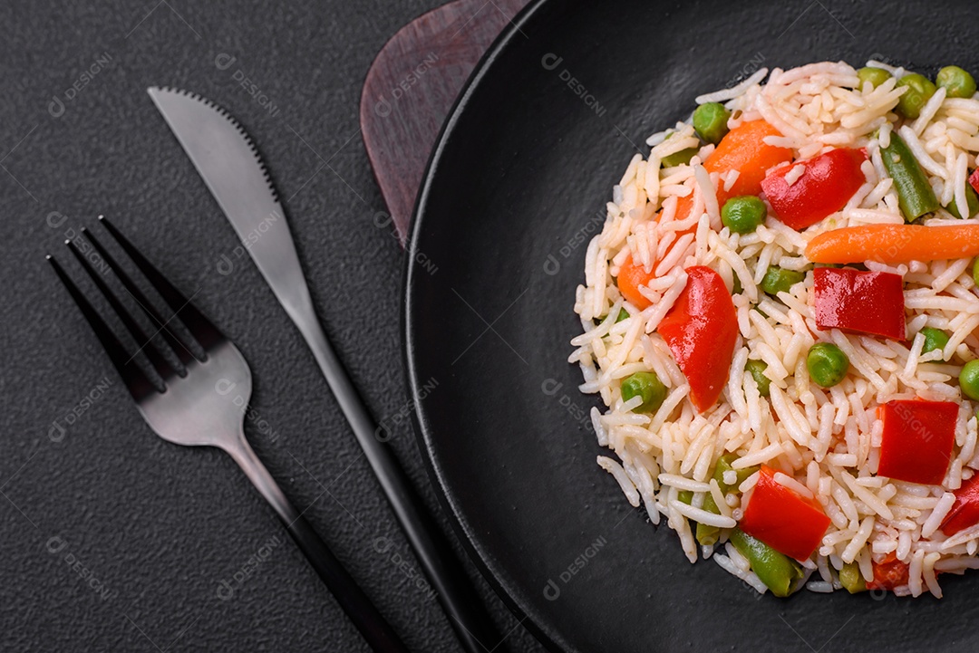 Delicioso arroz cozido com pimentão, ervilha, feijão de espargos e cenoura sobre um fundo de concreto texturizado