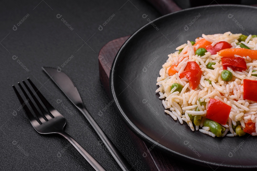 Delicioso arroz cozido com pimentão, ervilha, feijão de espargos e cenoura sobre um fundo de concreto texturizado