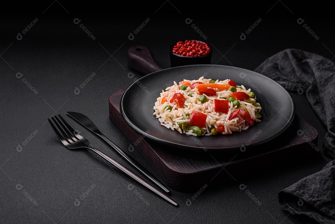 Delicioso arroz cozido com pimentão, ervilha, feijão de espargos e cenoura sobre um fundo de concreto texturizado