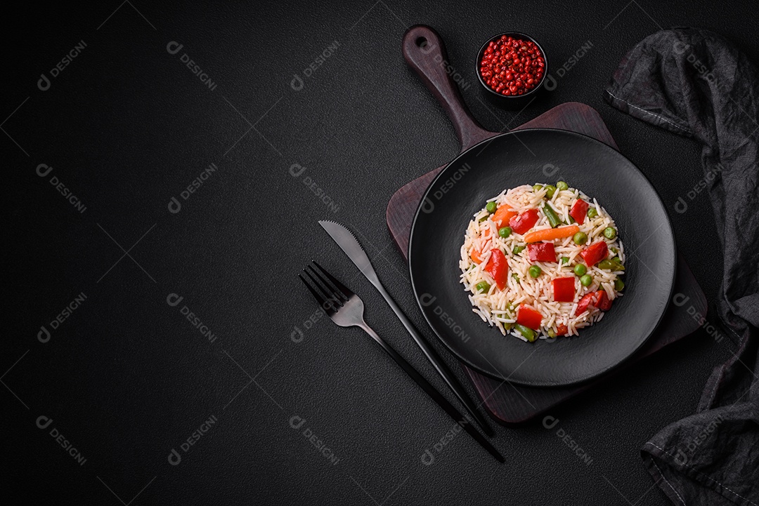 Delicioso arroz cozido com pimentão, ervilha, feijão de espargos e cenoura sobre um fundo de concreto texturizado