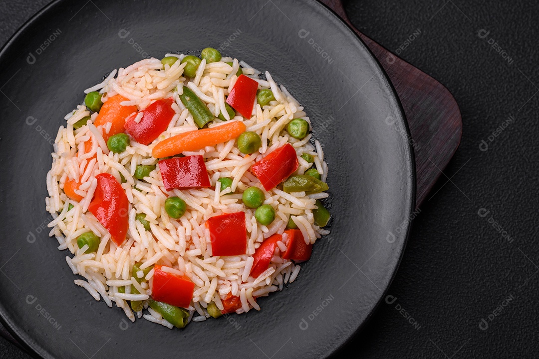 Delicioso arroz cozido com pimentão, ervilha, feijão de espargos e cenoura sobre um fundo de concreto texturizado