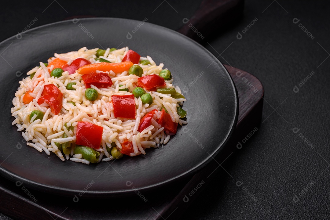 Delicioso arroz cozido com pimentão, ervilha, feijão de espargos e cenoura sobre um fundo de concreto texturizado