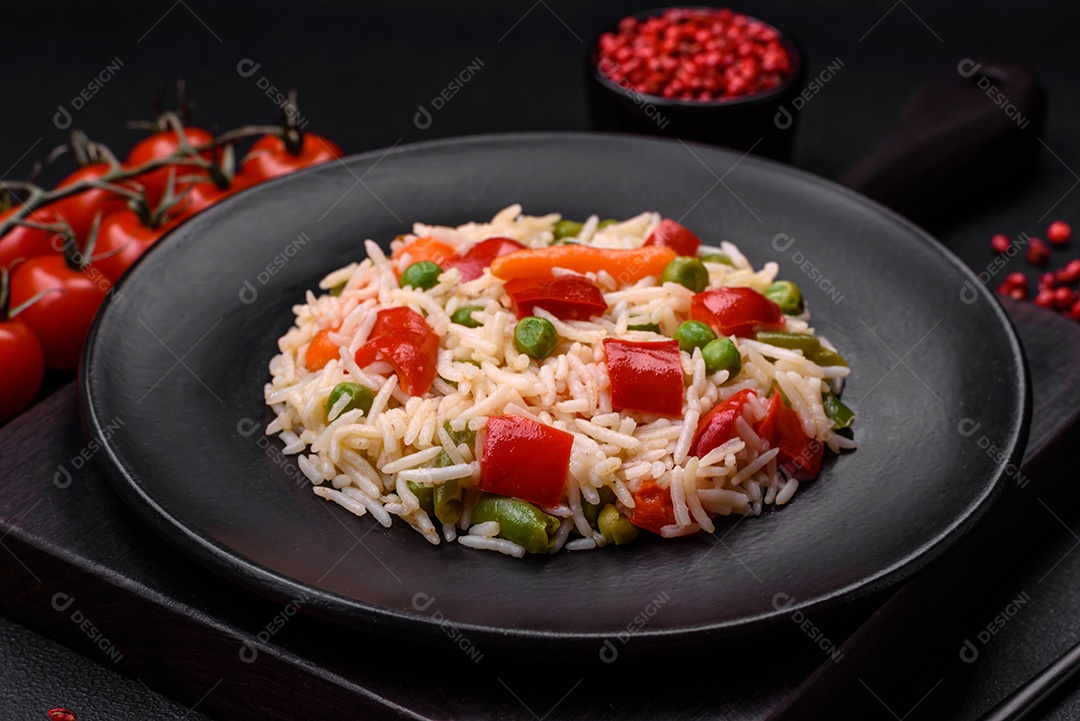 Delicioso arroz cozido com pimentão, ervilha, feijão de espargos e cenoura sobre um fundo de concreto texturizado