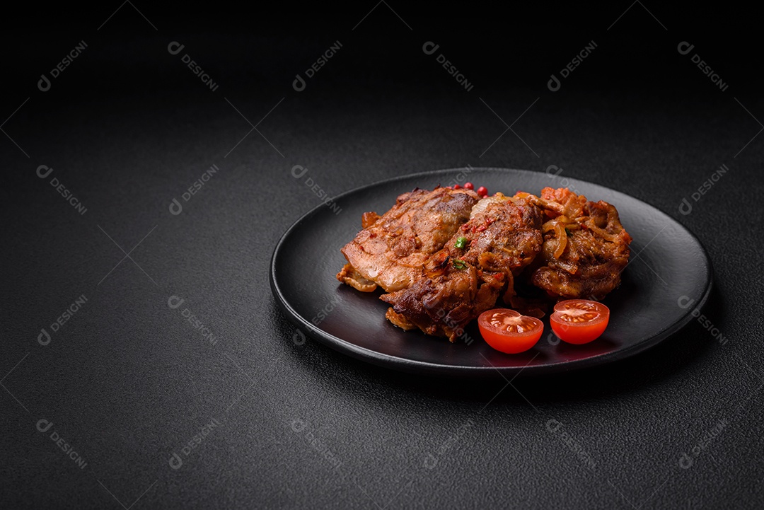 Delicioso frango frito em molho com cebola, sal, especiarias e ervas sobre um fundo escuro de concreto