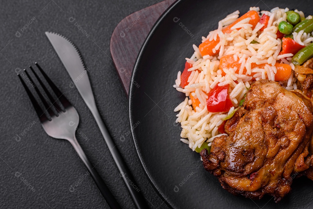 Delicioso arroz cozido com pimentão, ervilha, feijão de espargos e cenoura e frango frito sobre fundo de concreto texturizado