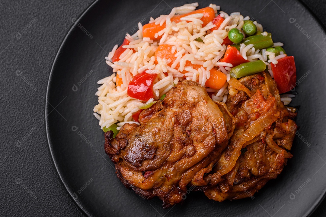 Delicioso arroz cozido com pimentão, ervilha, feijão de espargos e cenoura e frango frito sobre fundo de concreto texturizado