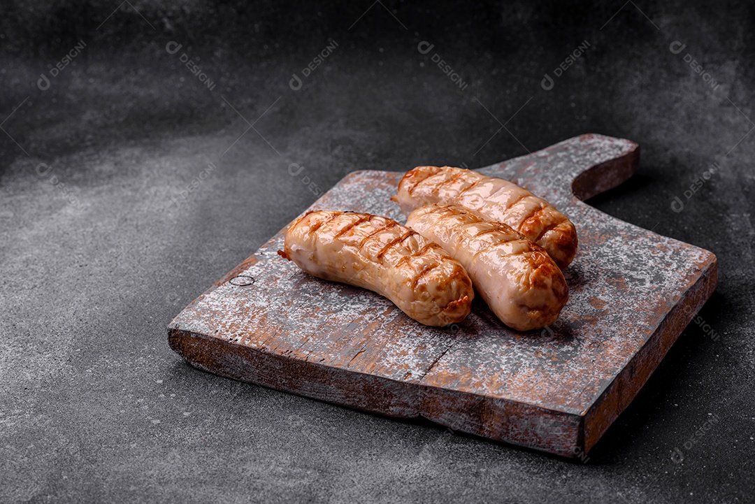 Deliciosas salsichas grelhadas de frango ou carne de porco com sal, especiarias e ervas sobre um fundo de concreto texturizado