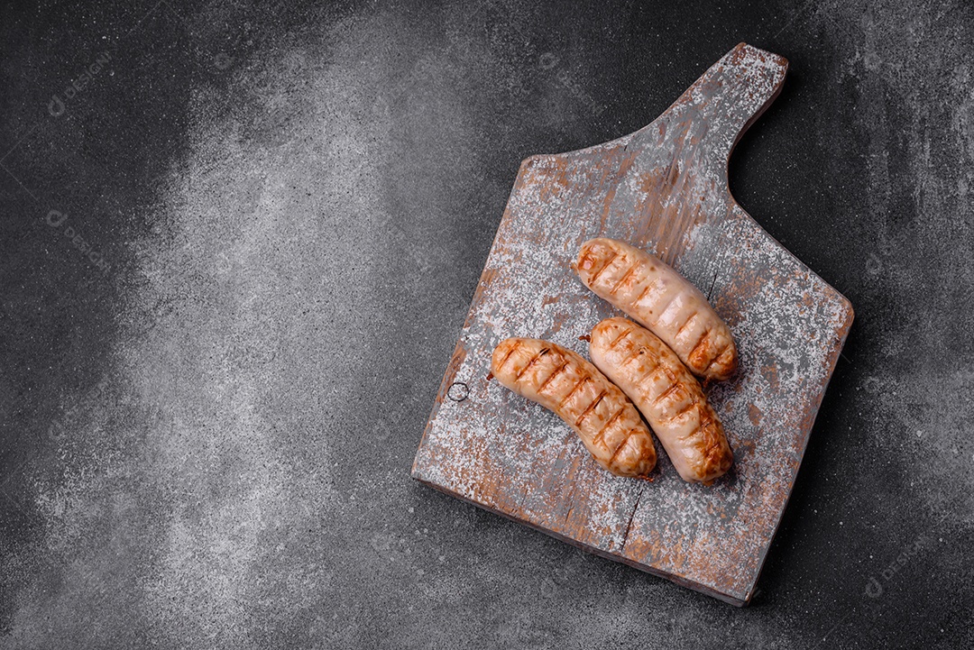 Deliciosas salsichas grelhadas de frango ou carne de porco com sal, especiarias e ervas sobre um fundo de concreto texturizado