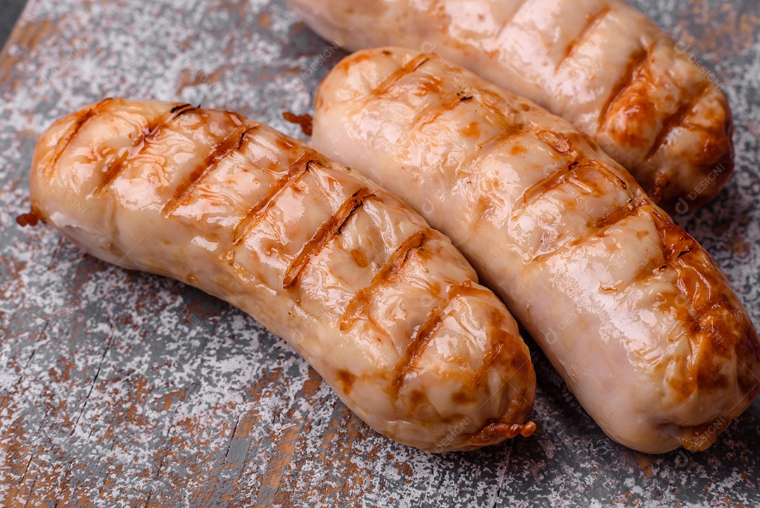 Deliciosas salsichas grelhadas de frango ou carne de porco com sal, especiarias e ervas sobre um fundo de concreto texturizado