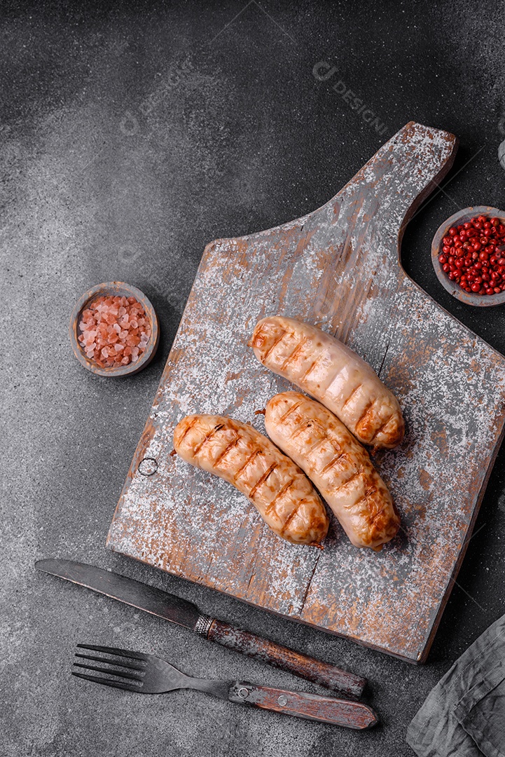Deliciosas salsichas grelhadas de frango ou carne de porco com sal, especiarias e ervas sobre um fundo de concreto texturizado