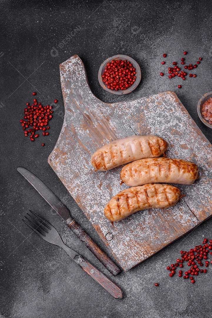 Deliciosas salsichas grelhadas de frango ou carne de porco com sal, especiarias e ervas sobre um fundo de concreto texturizado