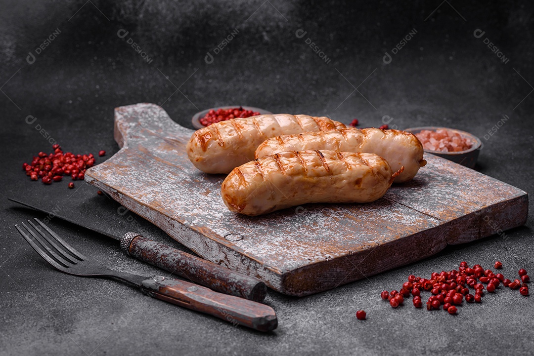 Deliciosas salsichas grelhadas de frango ou carne de porco com sal, especiarias e ervas sobre um fundo de concreto texturizado