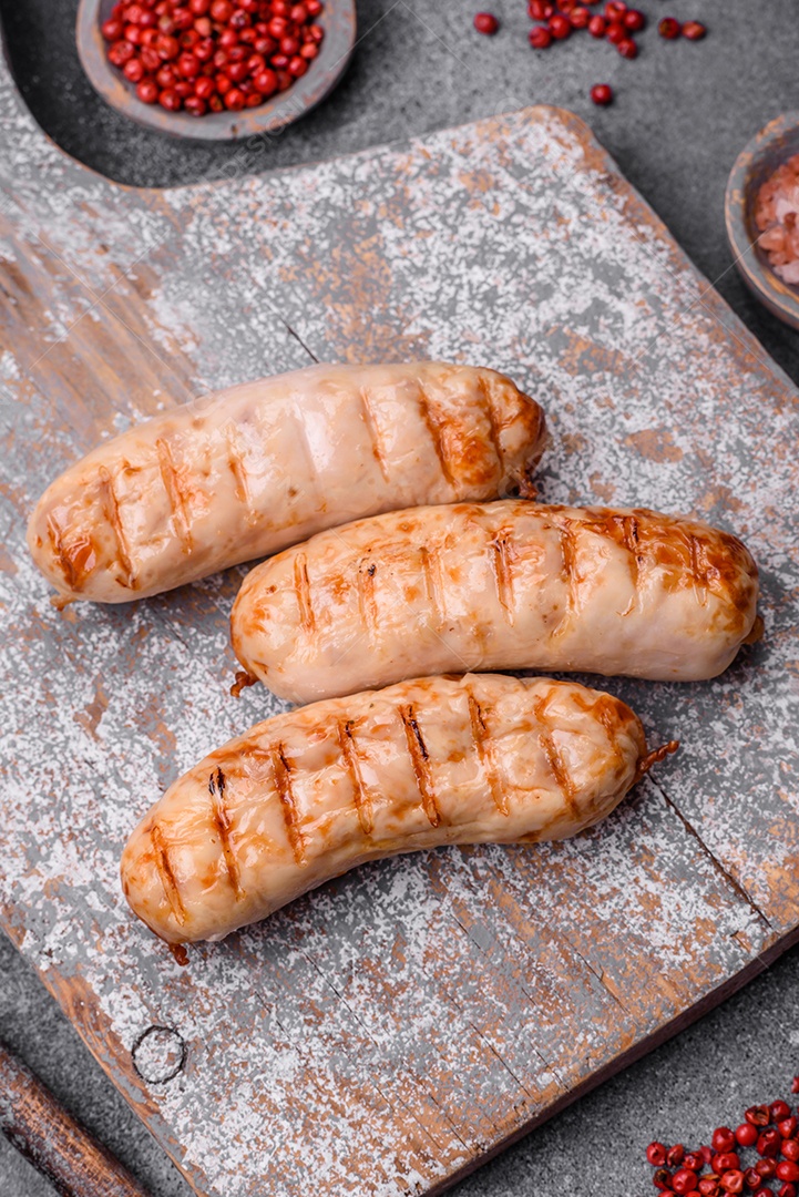 Deliciosas salsichas grelhadas de frango ou carne de porco com sal, especiarias e ervas sobre um fundo de concreto texturizado