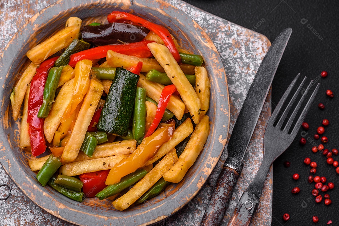 Deliciosas batatas fritas com pimentão, feijão de espargos, sal e especiarias em um prato sobre um fundo escuro de concreto