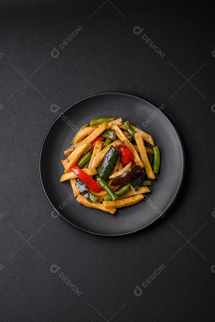 Deliciosas batatas fritas com pimentão, feijão de espargos, sal e especiarias em um prato sobre um fundo escuro de concreto