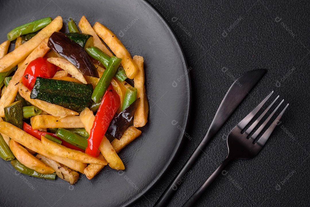 Deliciosas batatas fritas com pimentão, feijão de espargos, sal e especiarias em um prato sobre um fundo escuro de concreto