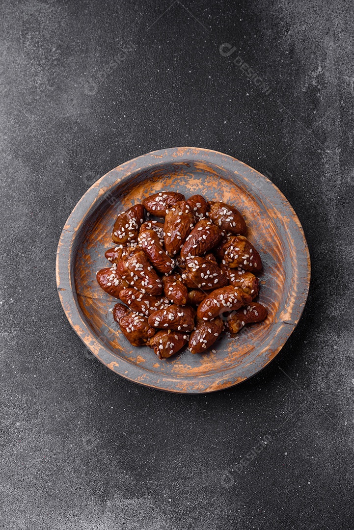 Corações de frango fritos em molho de soja com sal e especiarias em um prato sobre um fundo de concreto texturizado