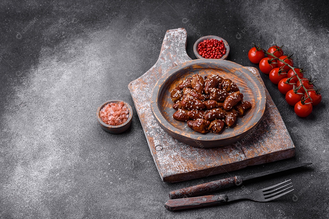 Corações de frango fritos em molho de soja com sal e especiarias em um prato sobre um fundo de concreto texturizado