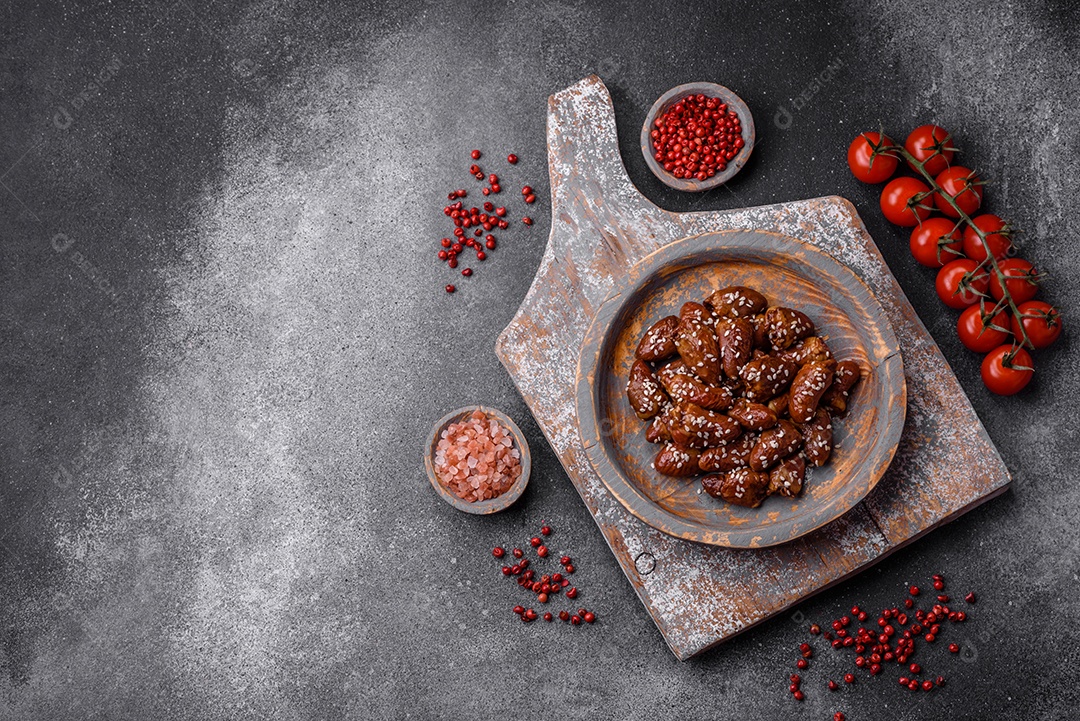 Corações de frango fritos em molho de soja com sal e especiarias em um prato sobre um fundo de concreto texturizado