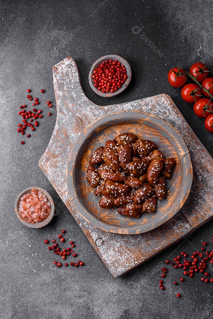 Corações de frango fritos em molho de soja com sal e especiarias em um prato sobre um fundo de concreto texturizado