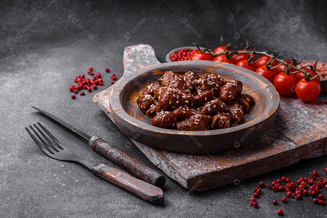Corações de frango fritos em molho de soja com sal e especiarias em um prato sobre um fundo de concreto texturizado