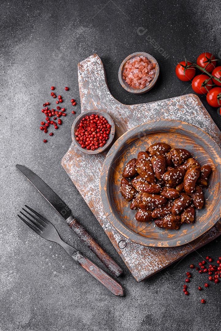 Corações de frango fritos em molho de soja com sal e especiarias em um prato sobre um fundo de concreto texturizado
