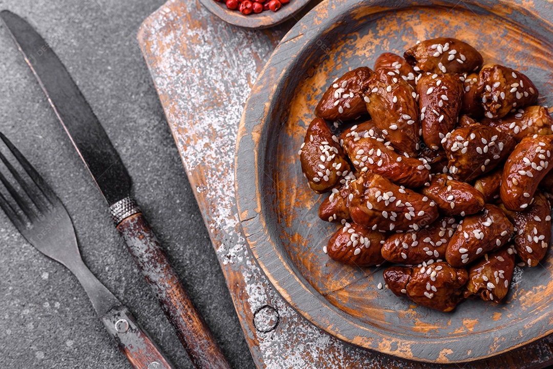 Corações de frango fritos em molho de soja com sal e especiarias em um prato sobre um fundo de concreto texturizado