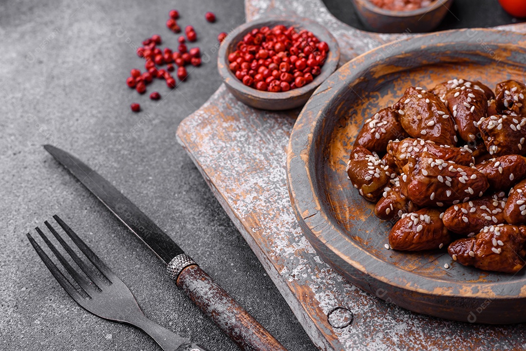 Corações de frango fritos em molho de soja com sal e especiarias em um prato sobre um fundo de concreto texturizado