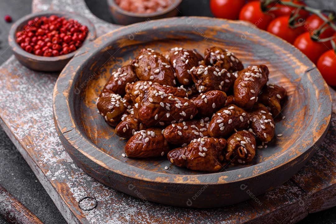 Corações de frango fritos em molho de soja com sal e especiarias em um prato sobre um fundo de concreto texturizado