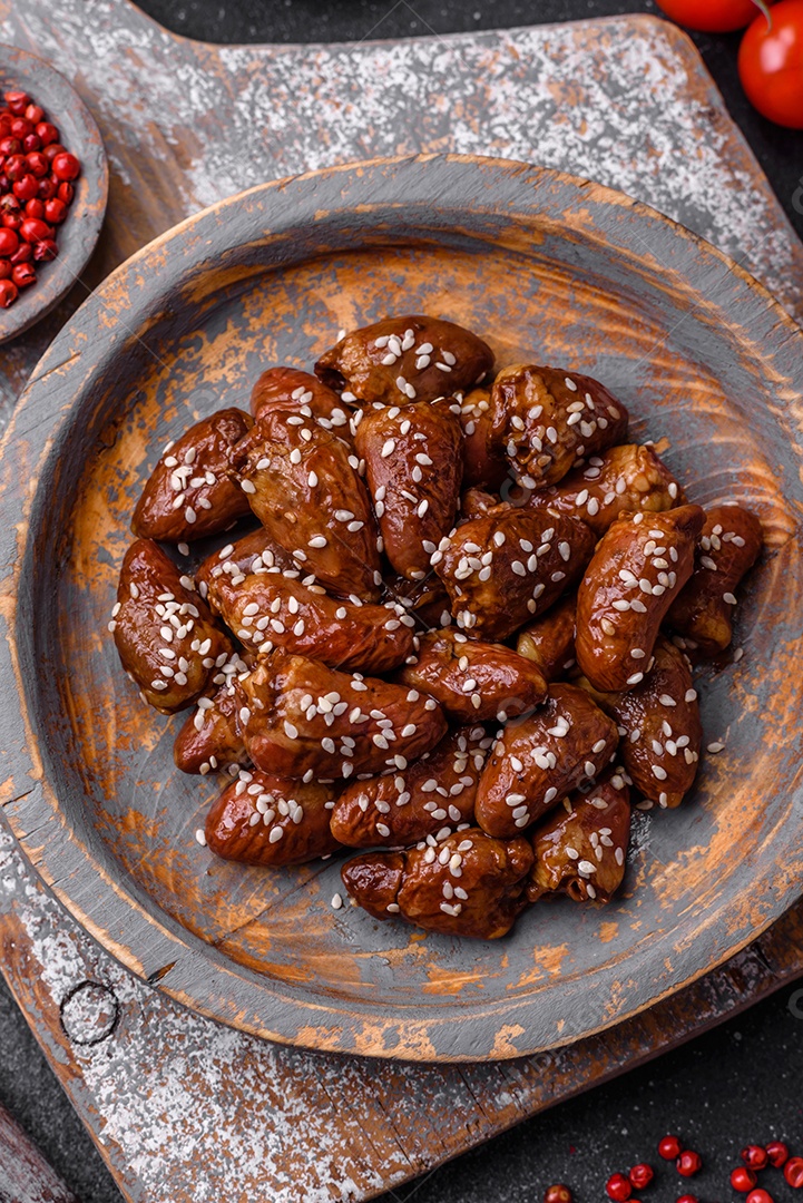Corações de frango fritos em molho de soja com sal e especiarias em um prato sobre um fundo de concreto texturizado